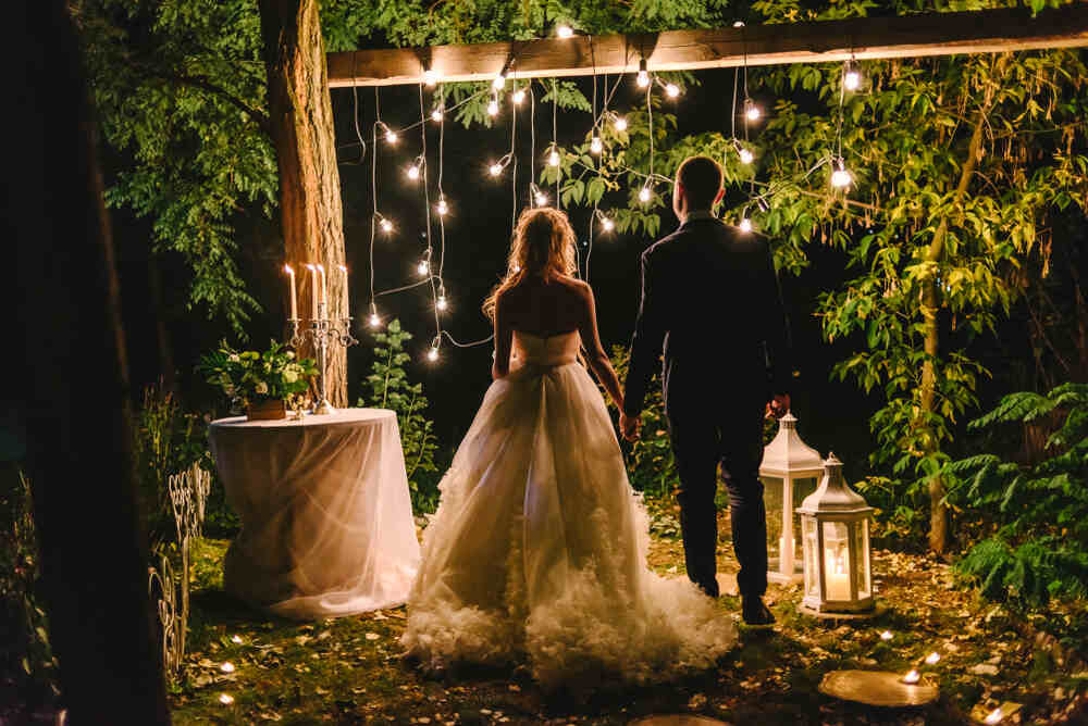 A bride and groom are surrounded by lights and lanterns during their summertime evening wedding