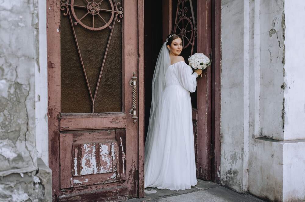 A bride in a vintage wedding gown poses outside of a timeless venue