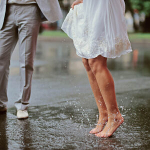 A barefoot bride splashes in a puddle beside her groom 