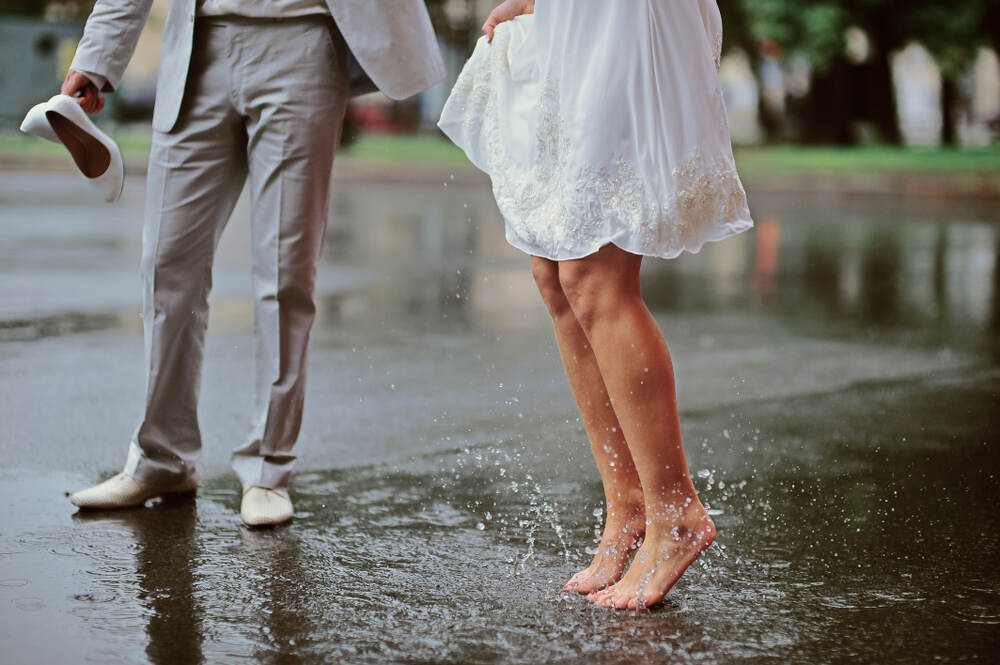 A barefoot bride splashes in a puddle beside her groom