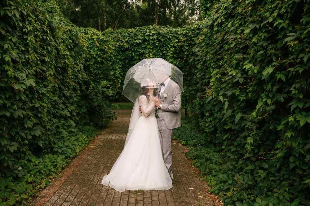 A bride and groom kiss under a translucent umbrella